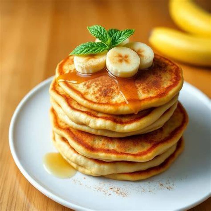 Banana pancakes on a white plate topped with sliced banana.