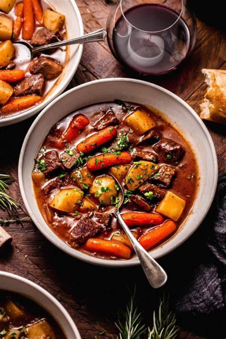 Beef stew and red wine with a loaf of bread in the background.