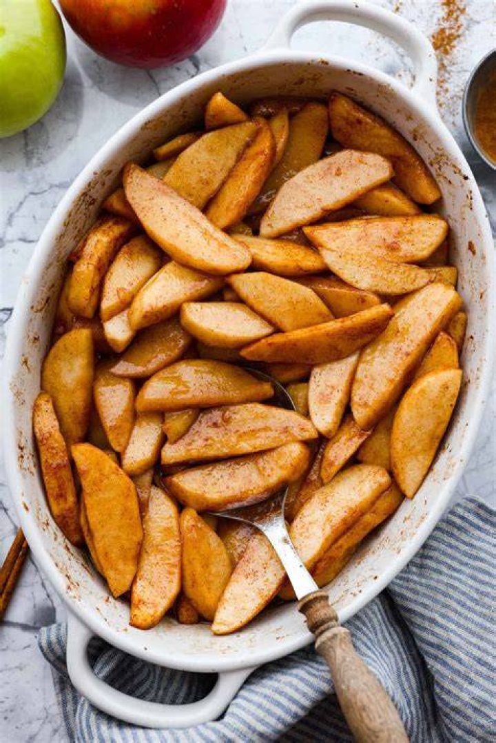 Sliced apples, cinnamon, and sugar in a glass bowl.
