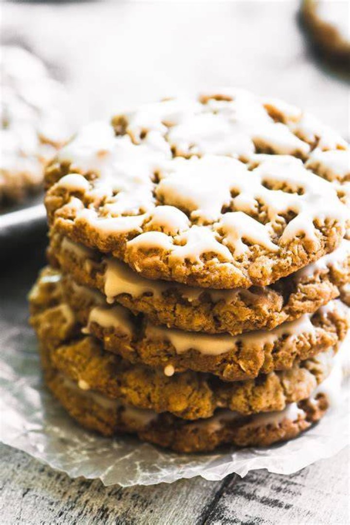 Stack of maple oatmeal cookies surrounded by oats and a spoon filled with syrup.